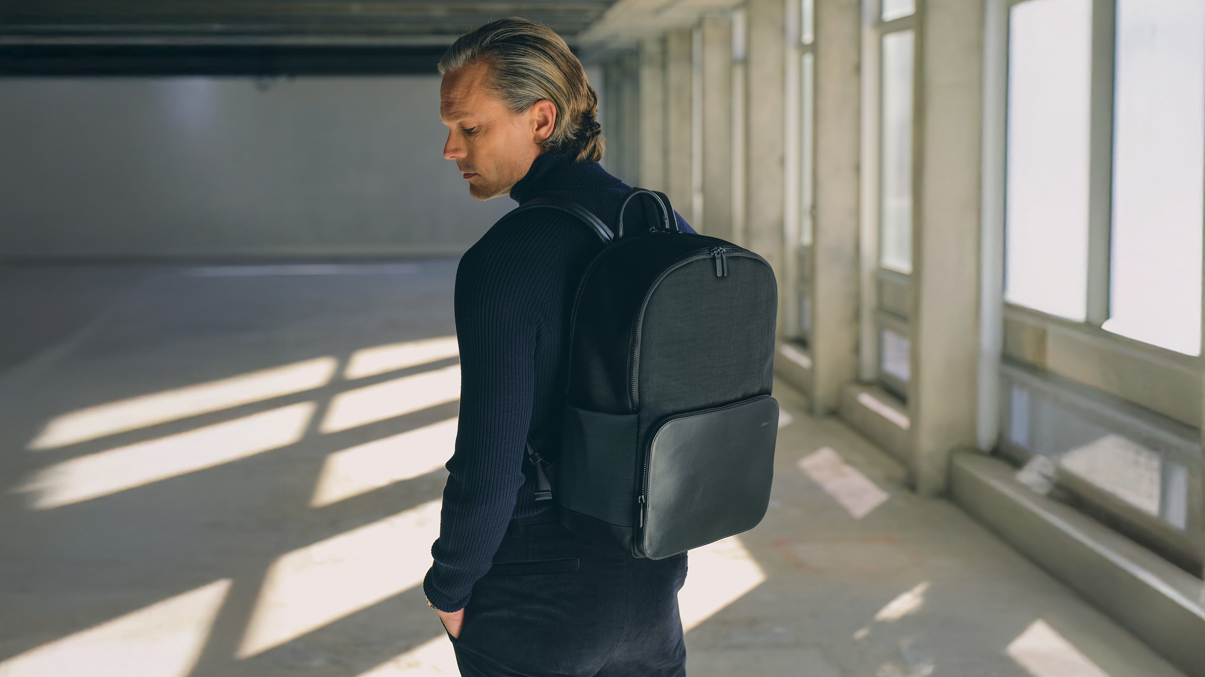 Model wearing black executive backpack for men in a modern workspace setting